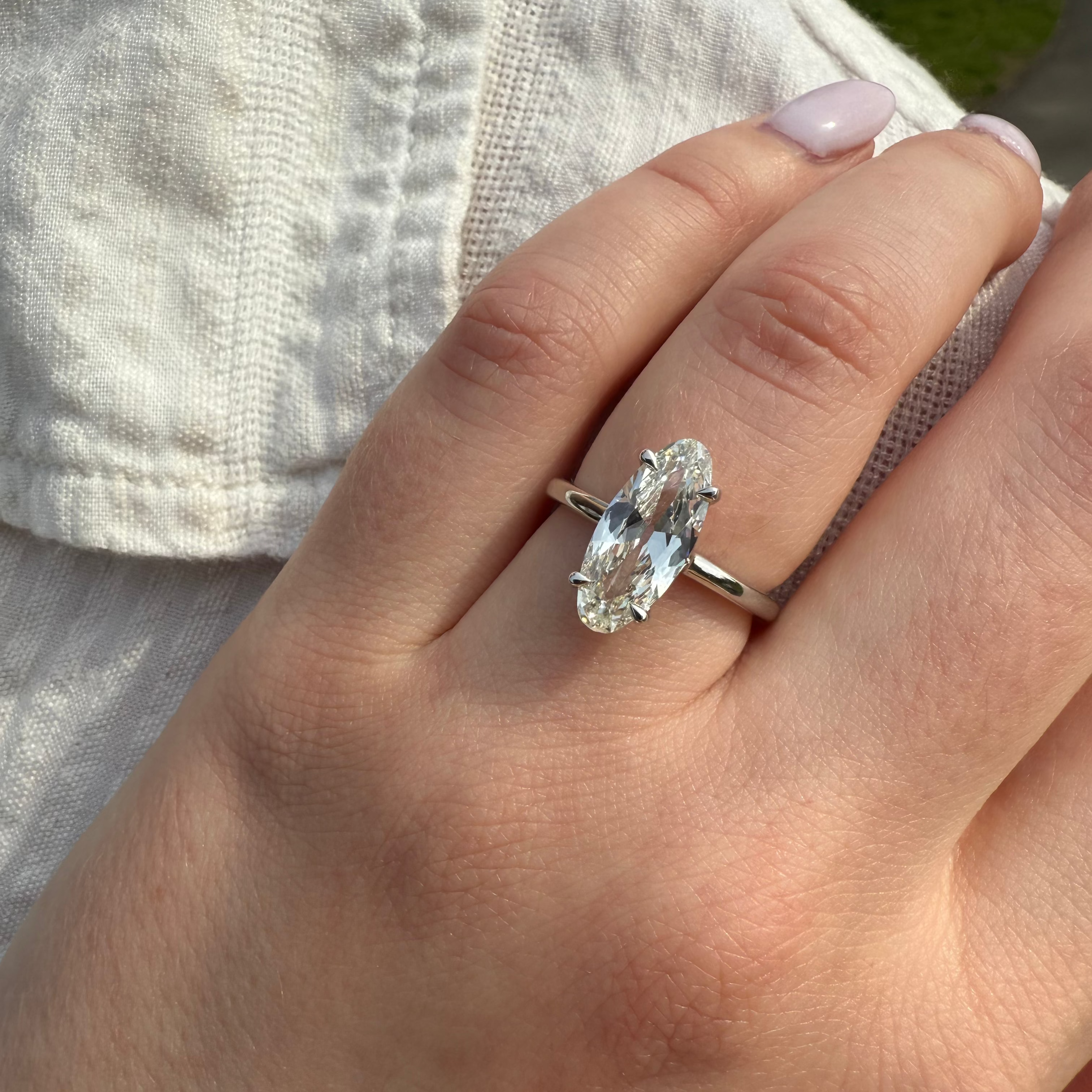 Hand wearing a silver ring with a white diamond against a neutral background
