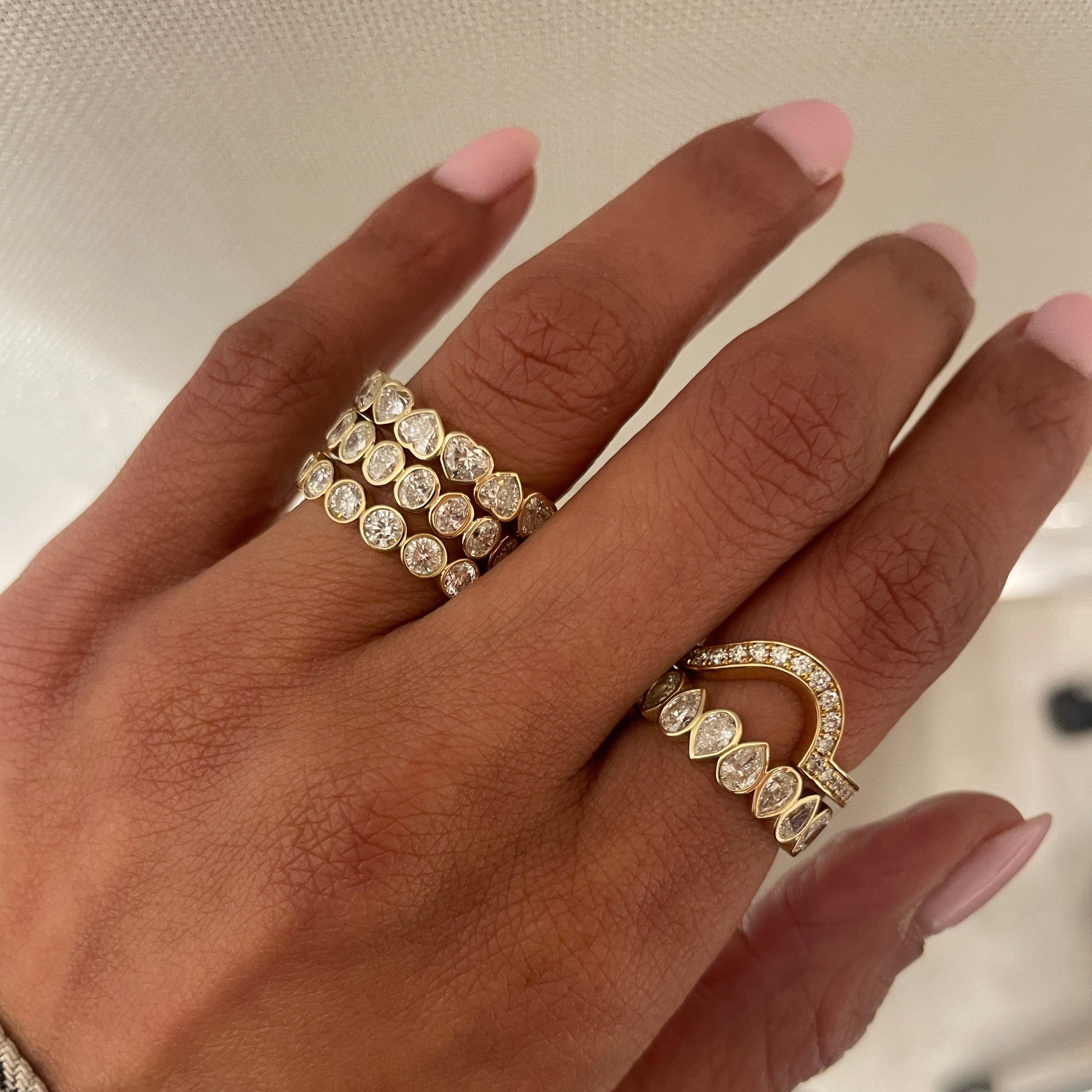 Fortuna round brilliant band on hand with fides heart and flora oval eternity bands in 18 kt yellow gold.