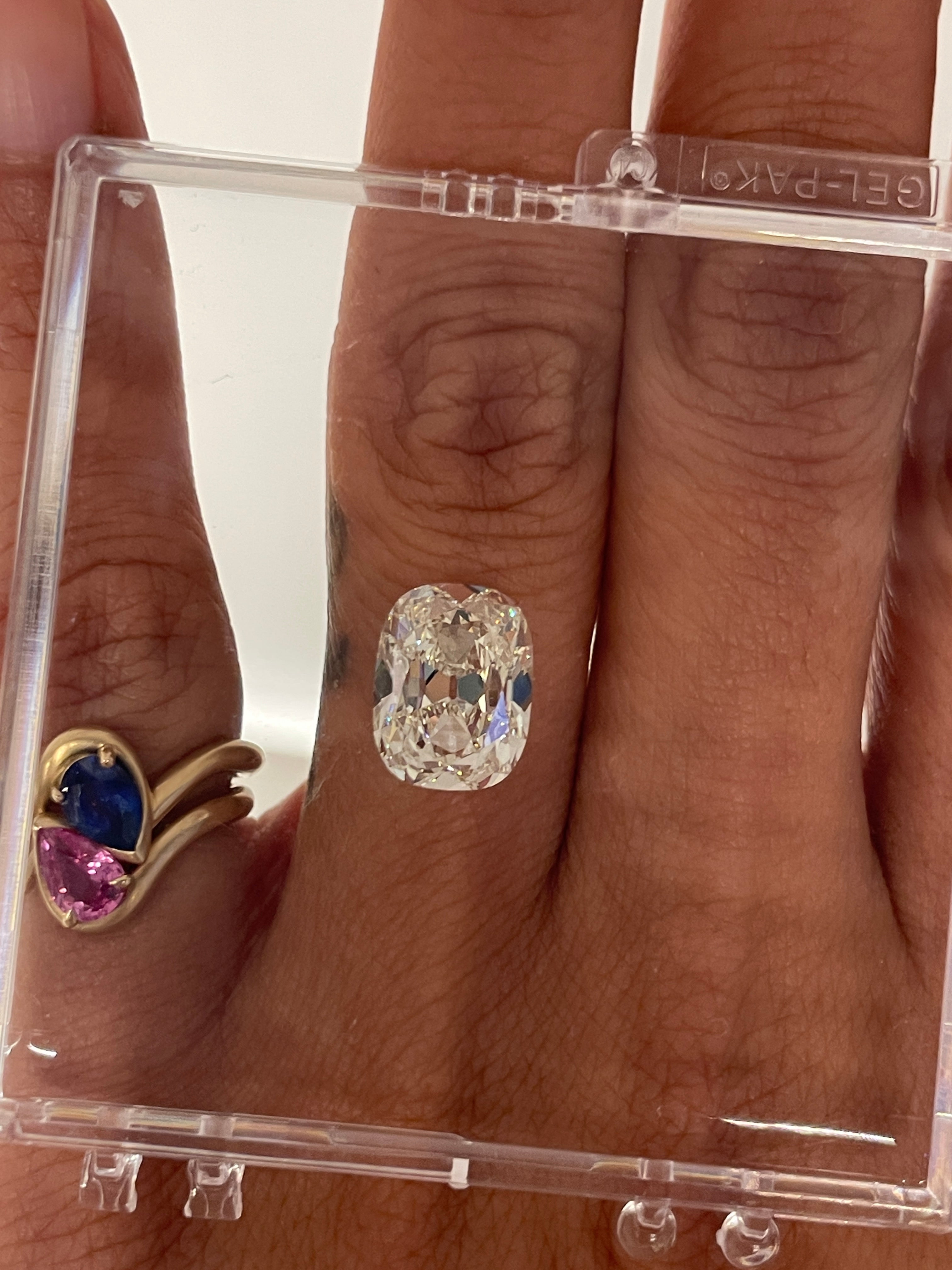 Close-up of a hand wearing a cushion diamond with a clear plastic display case. BB thelma Blue and Pink Sapphire Stacked on the pinky finger. 