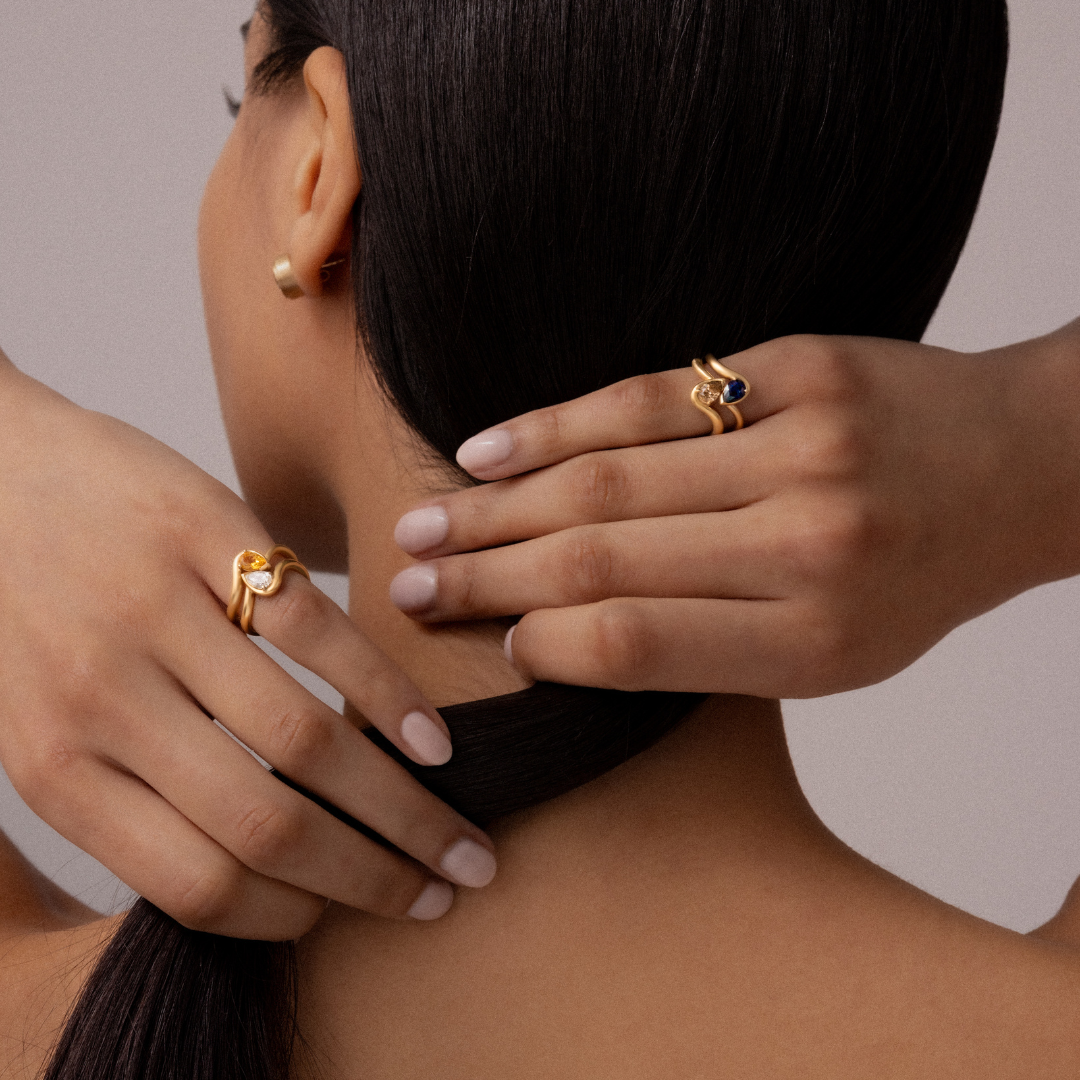 Hand model wearing BB Thelma pink rings in citrine, diamond, blue sapphire, and brown diamond. 14k yellow gold